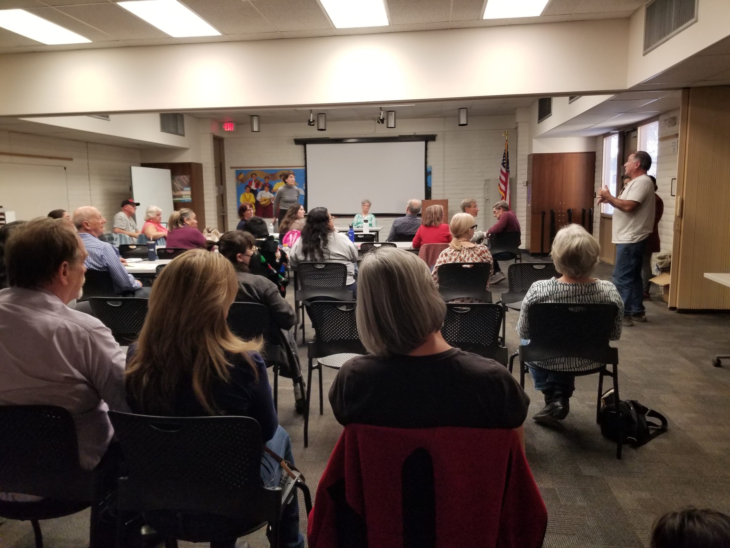 Image of the backs of people's heads sitting in chairs, with one man standing and speaking.