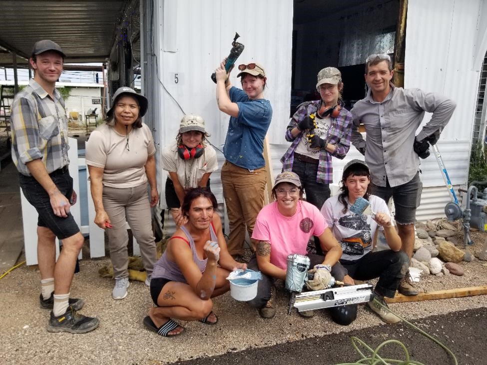 Poder Casas Moviles volunteer pose with tools and paint brushes outside of mobile home they are repairing.